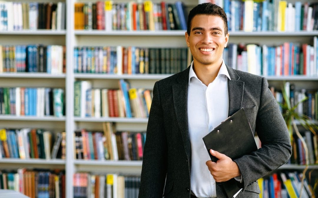 smiling-man-holding-clipboard-in-front-of-bookshelf