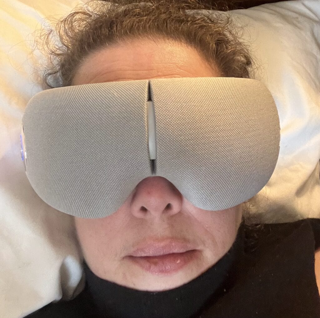 Person wearing a FSA eligible eye massager, resting on a pillow for relaxation.