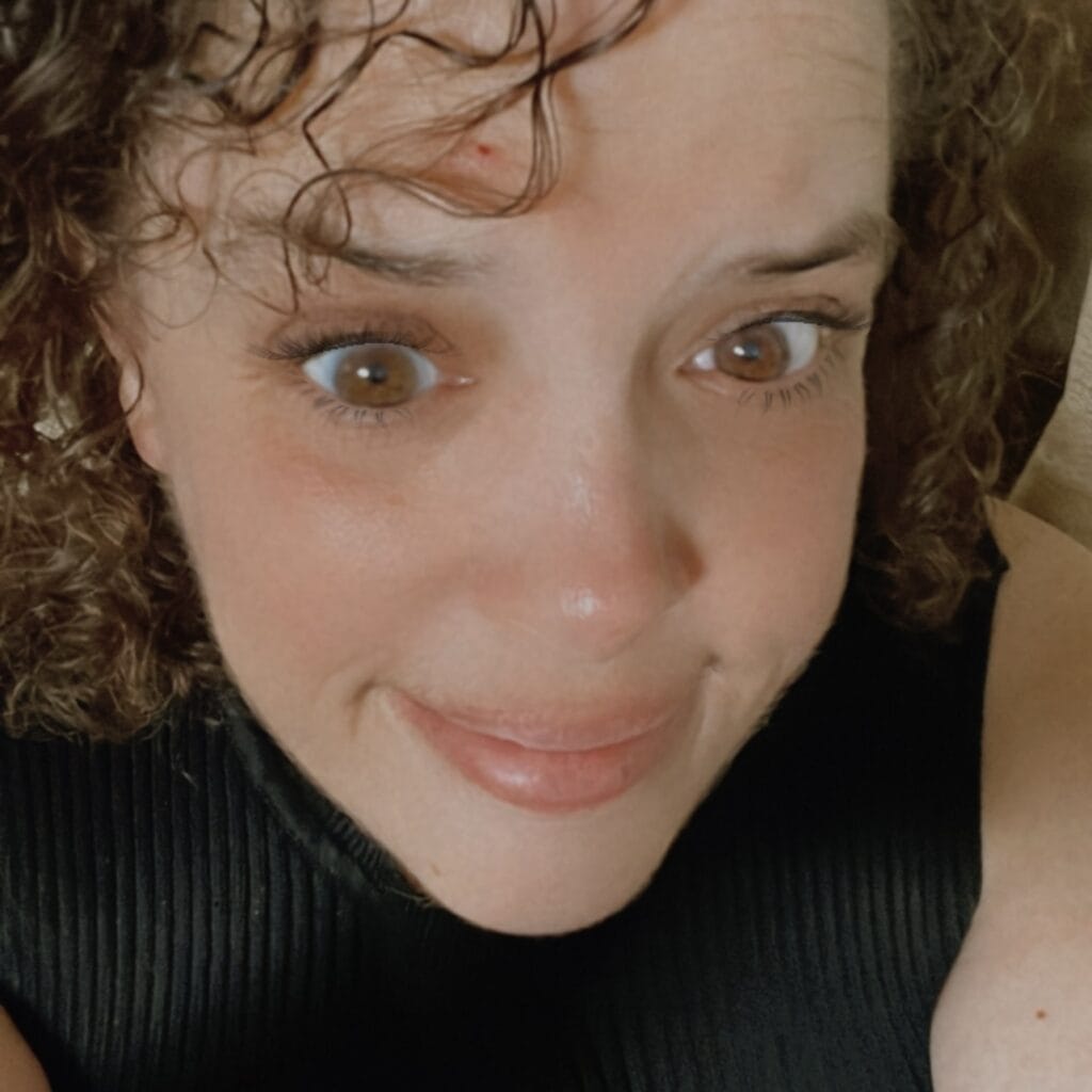 Close-up of a woman with curly hair and brown eyes smiling at the camera.
