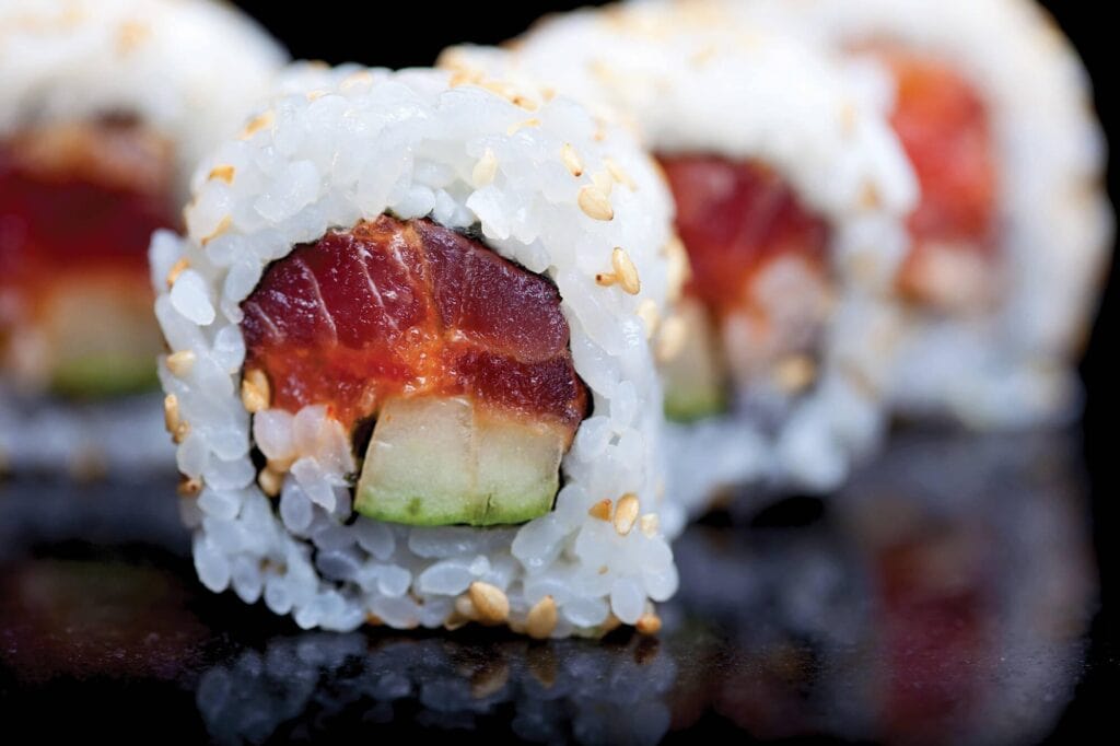 Close-up of a sushi roll with tuna, cucumber, and sesame seeds.