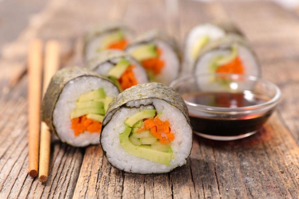 Close-up of vegetable sushi rolls with soy sauce on rustic wooden table.