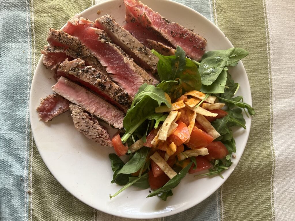 Seared tuna steak with mixed greens and vegetable salad on white plate.