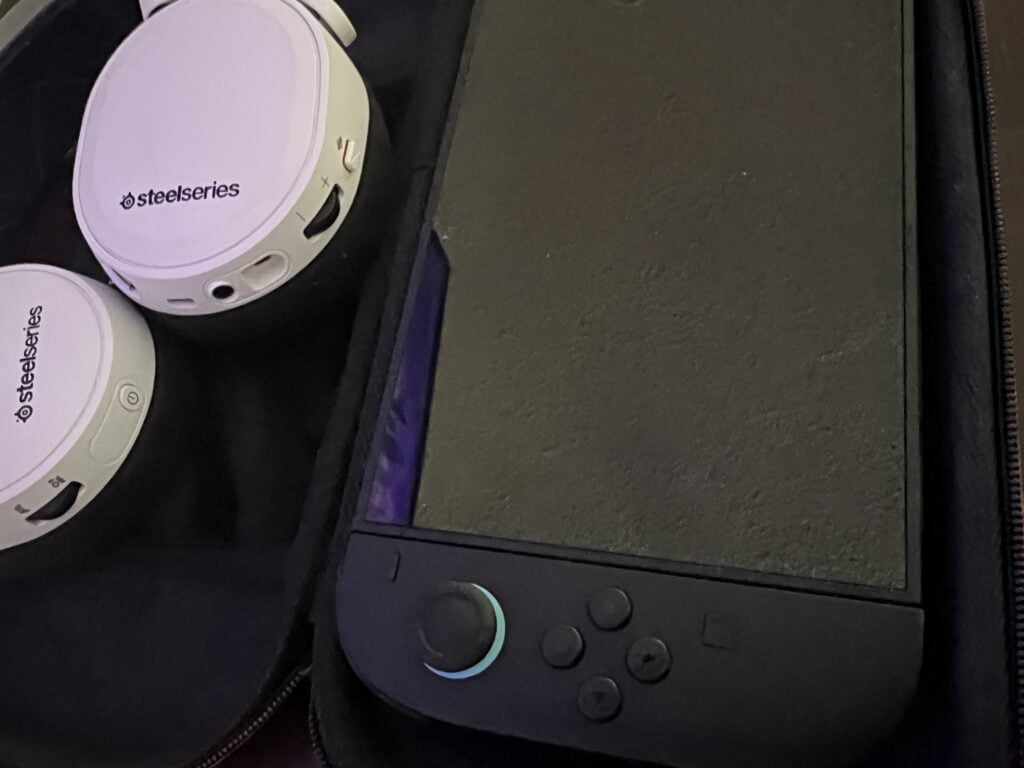 Wireless SteelSeries headphones and a portable device on a black surface.