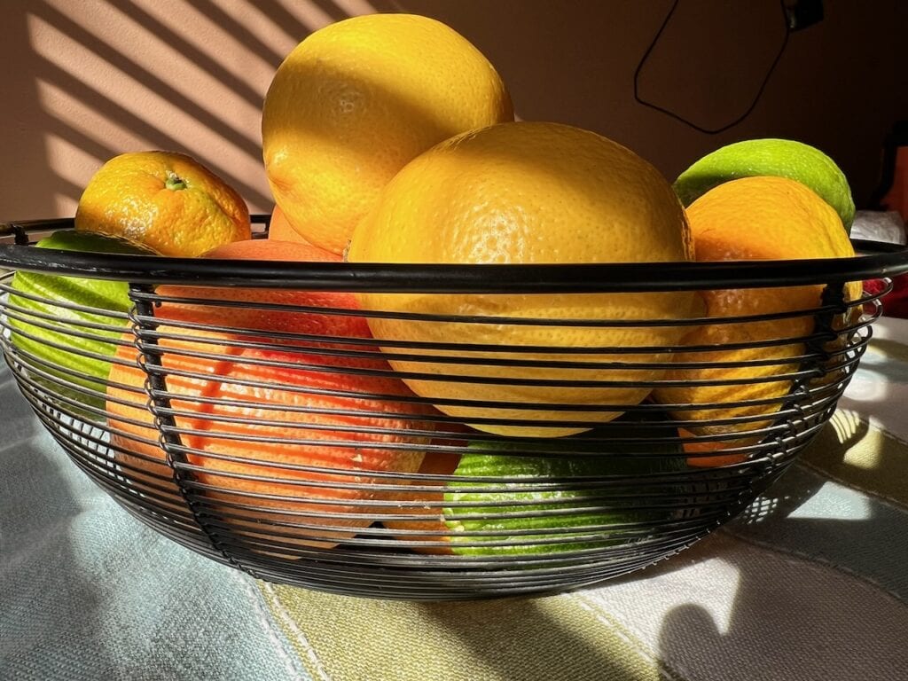 Vibrant citrus fruits in a black wire basket on a sunlit table.
