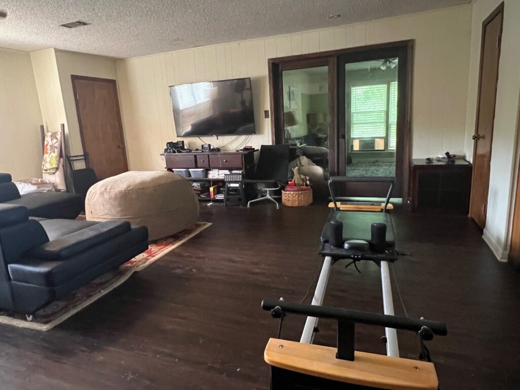 Living room with TV, black sofas, and workout bench on dark wood floor.