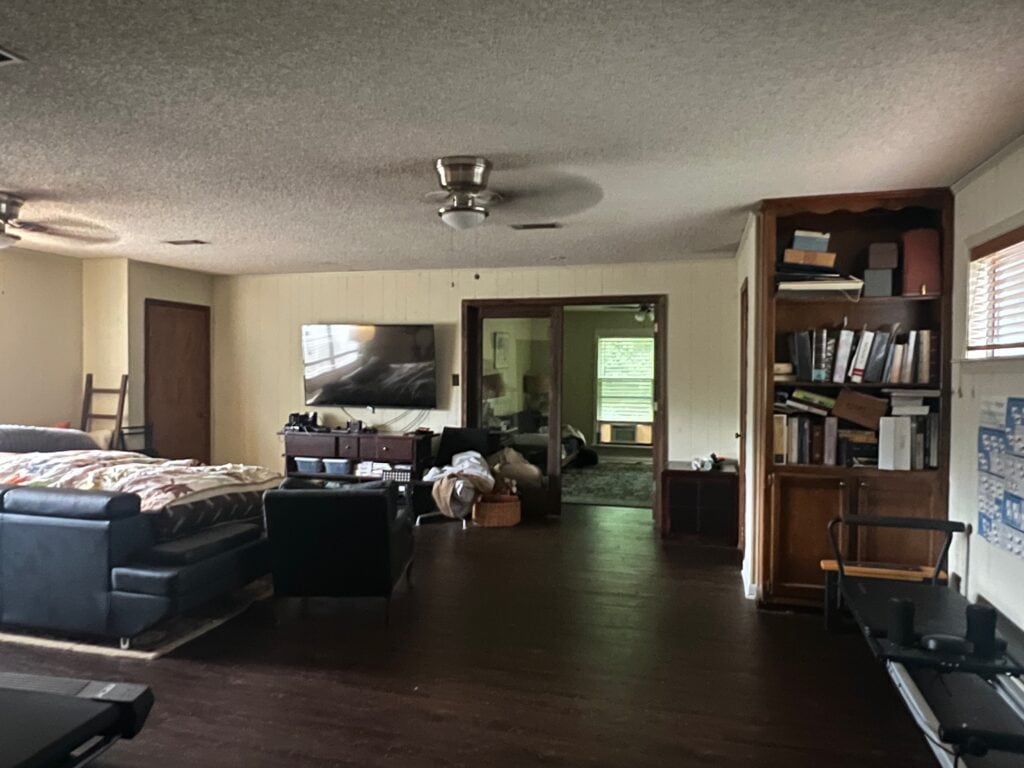 Spacious living room with dark wood flooring, TV, and bookshelf.