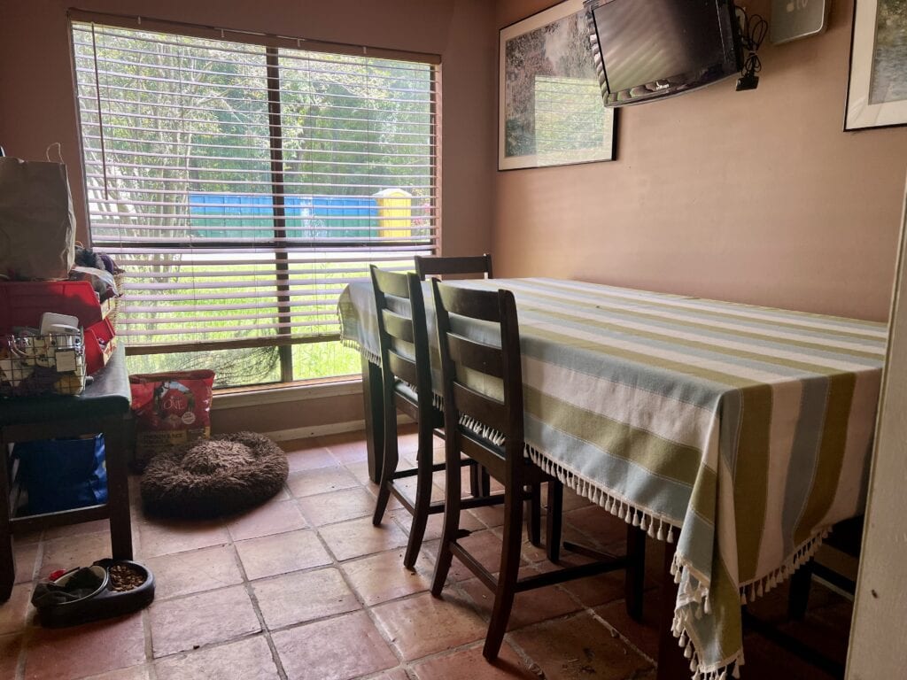 Bright dining space with striped tablecloth, large window, and wall-mounted TV.