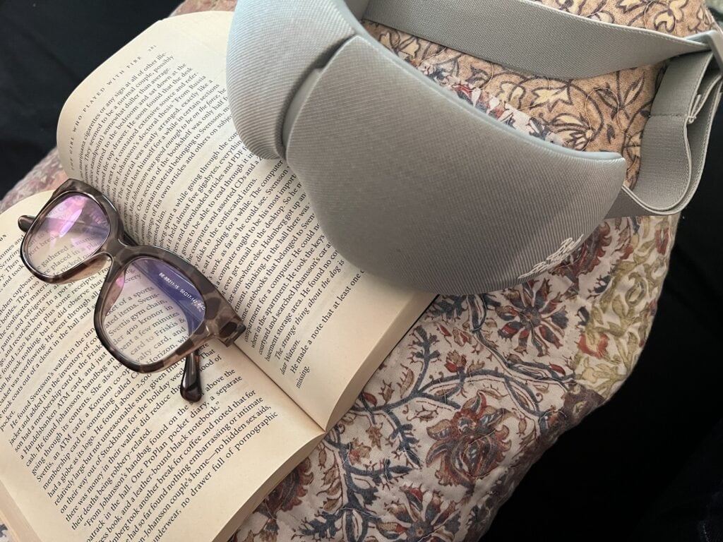 Open book, glasses, and bag on a floral blanket.