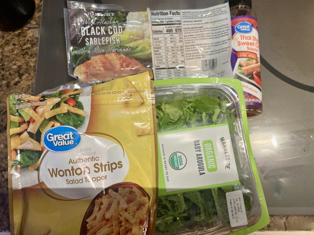 Assorted food packages including salad, sauce, and fish fillet on a kitchen counter.