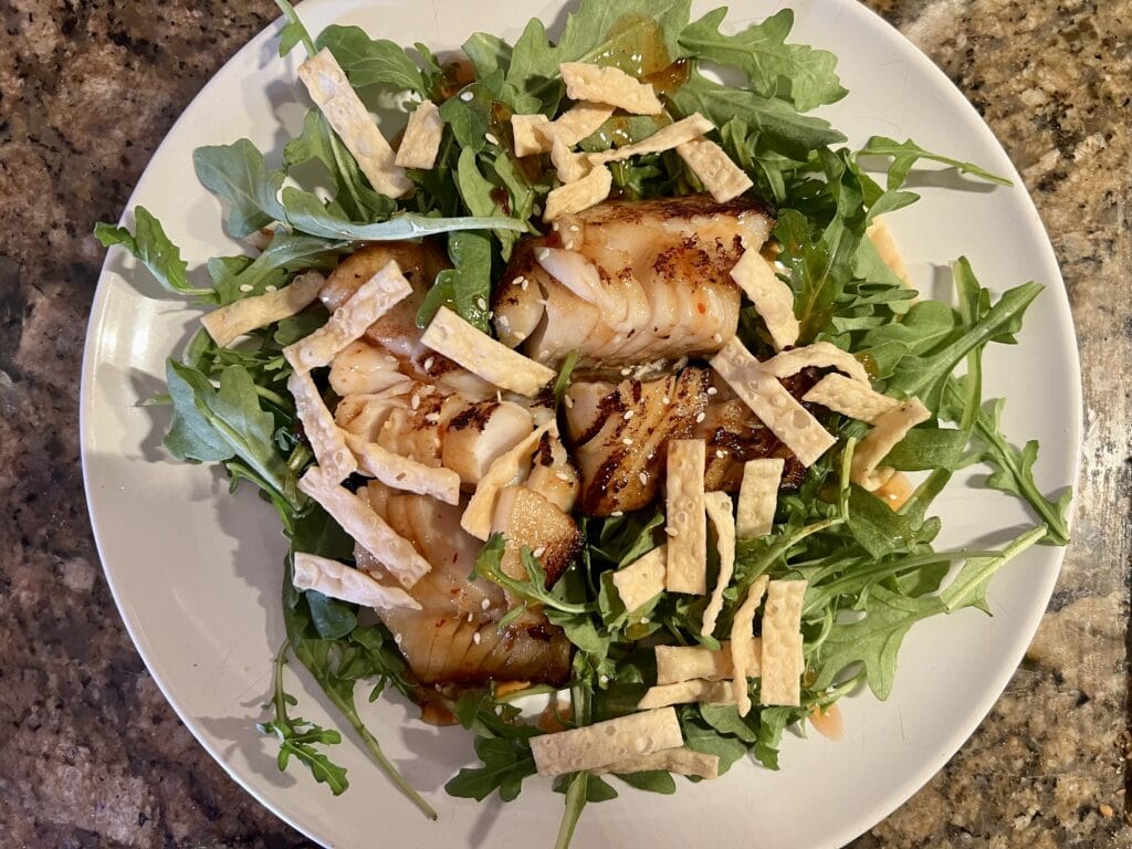 Delicious fish salad with arugula, crispy toppings, and dressing on a white plate.