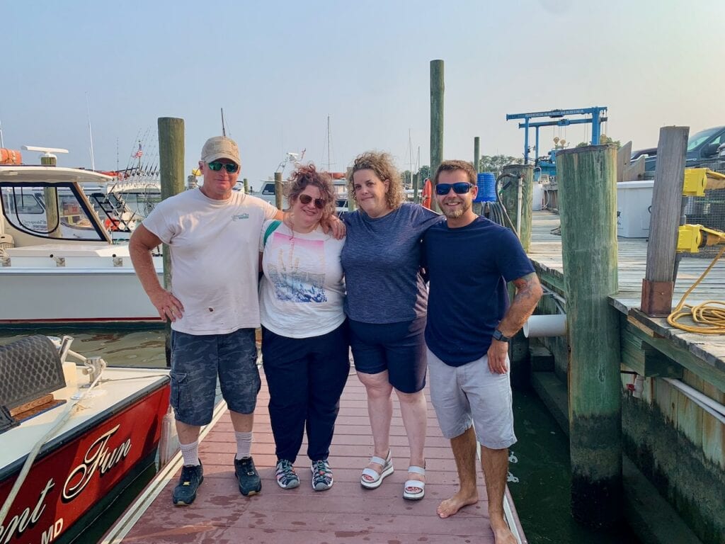 Four friends standing on a marina dock with boats in the background.