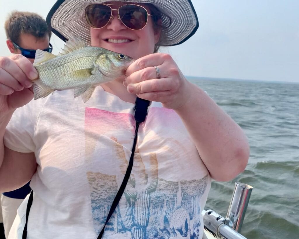 Woman holding a fish on a boat during a fishing trip at sea.