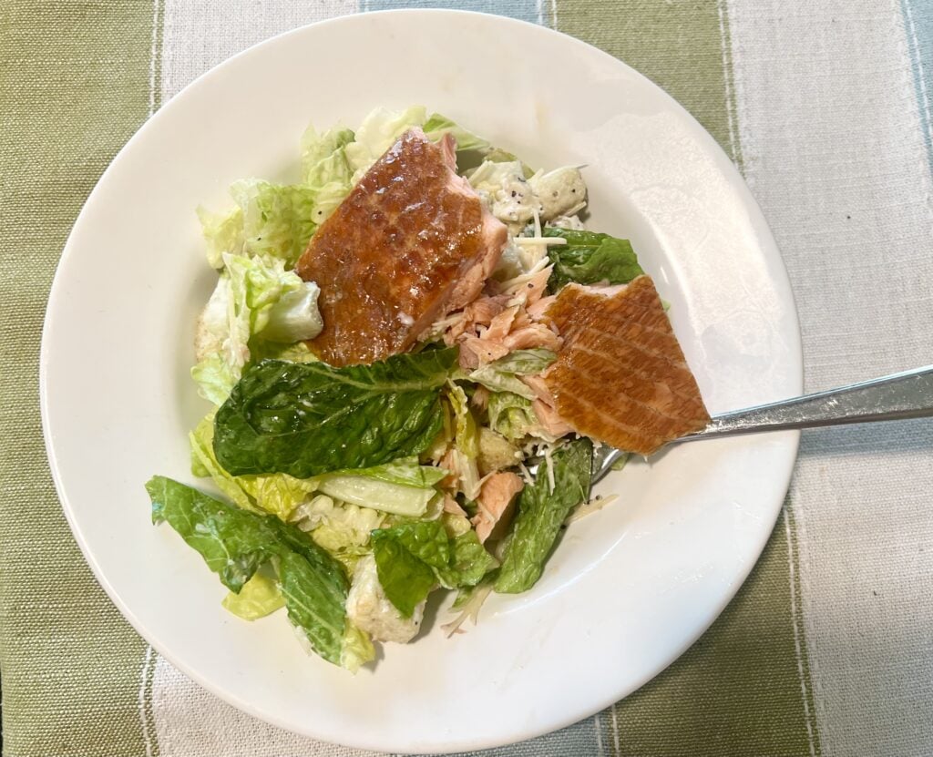 Fresh salmon salad with lettuce, greens, and dressing on a white plate.