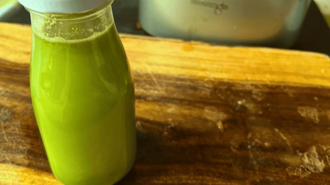 Fresh green juice in a glass bottle on a wooden surface.