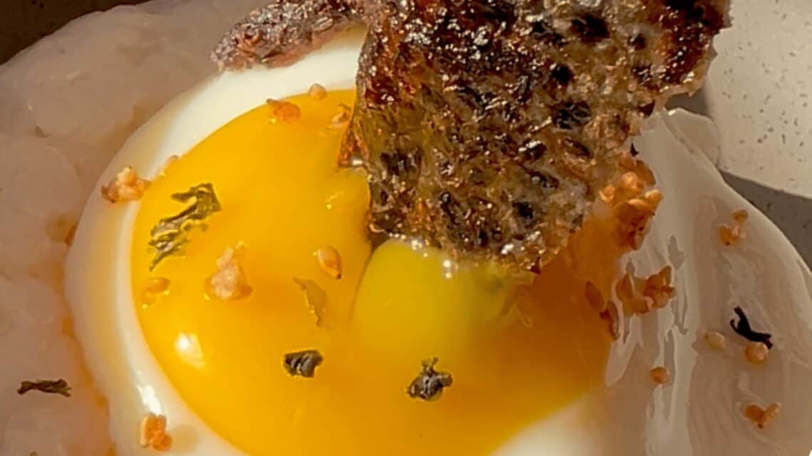 Gourmet breakfast with fried egg, crispy bacon, and toast, showcasing delicious food presentation.