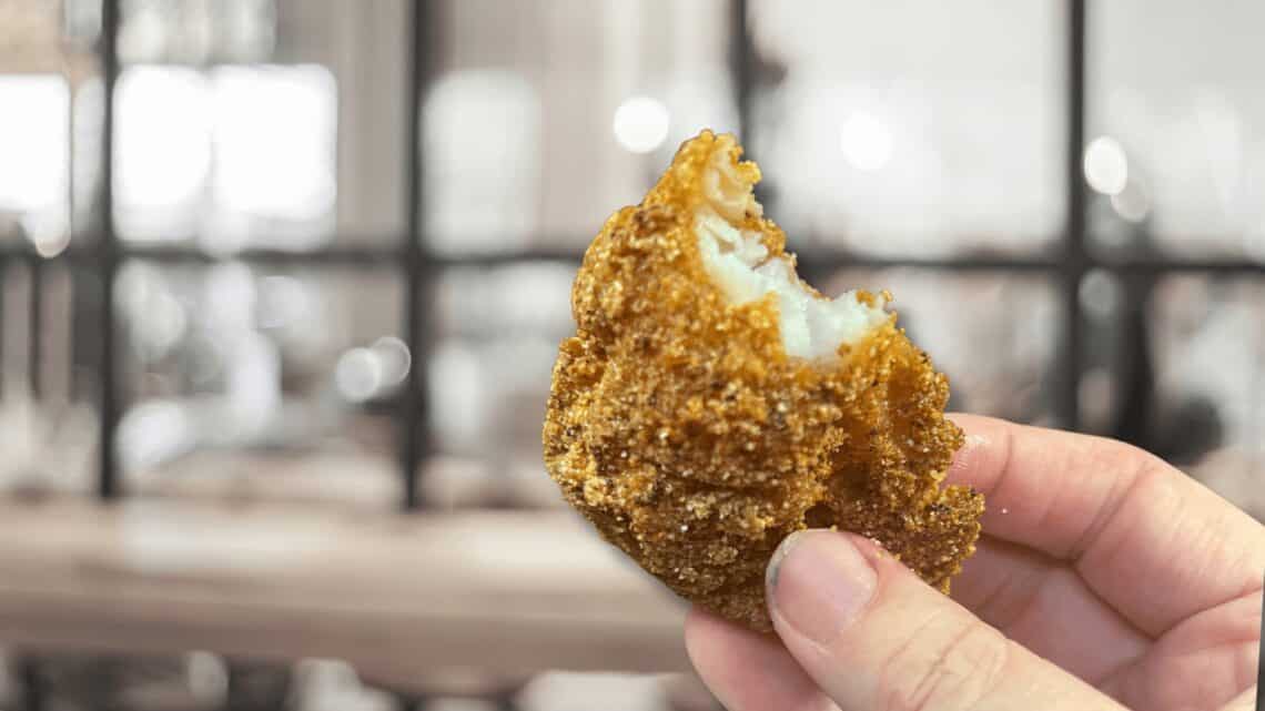 Delicious golden-brown croquette held in hand, showcasing crispy exterior and creamy filling.