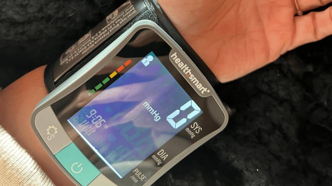 Digital wrist blood pressure monitor showing systolic, diastolic, and pulse readings with app connec.