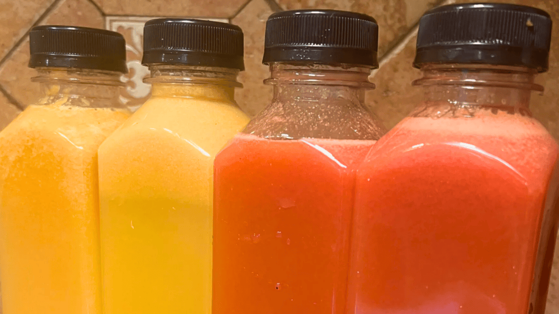 Four bottles of juice or smoothie with black caps in yellow, orange, and pink colors.