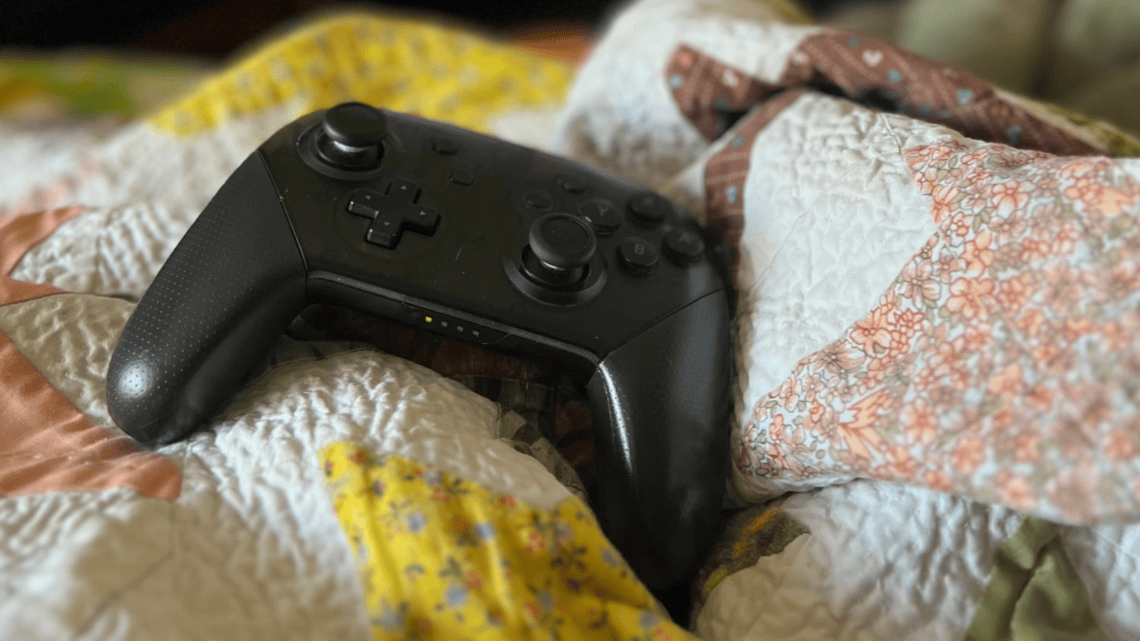Nintendo Pro Controller resting on a colorful quilt bed.