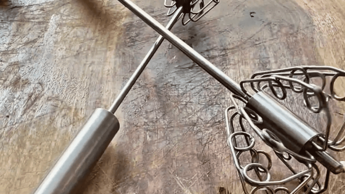 Two push whisks resting on a rustic wooden table.