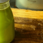 Fresh green juice in a glass bottle on a wooden surface.