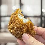 Delicious golden-brown croquette held in hand, showcasing crispy exterior and creamy filling.