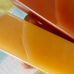 Glass bottle of fresh orange juice with a brown tray in the background.