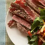 Juicy homemade steak with fresh greens and tomato salad on a white plate.