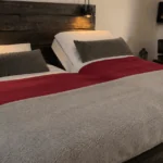 Cozy bedroom with wooden headboard, red and gray bedding, and ambient lighting.