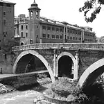 Historic stone bridge over a river in a cityscape, black and white photo.