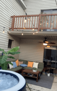Outdoor patio with seating, string lights, and a hot tub under a balcony.