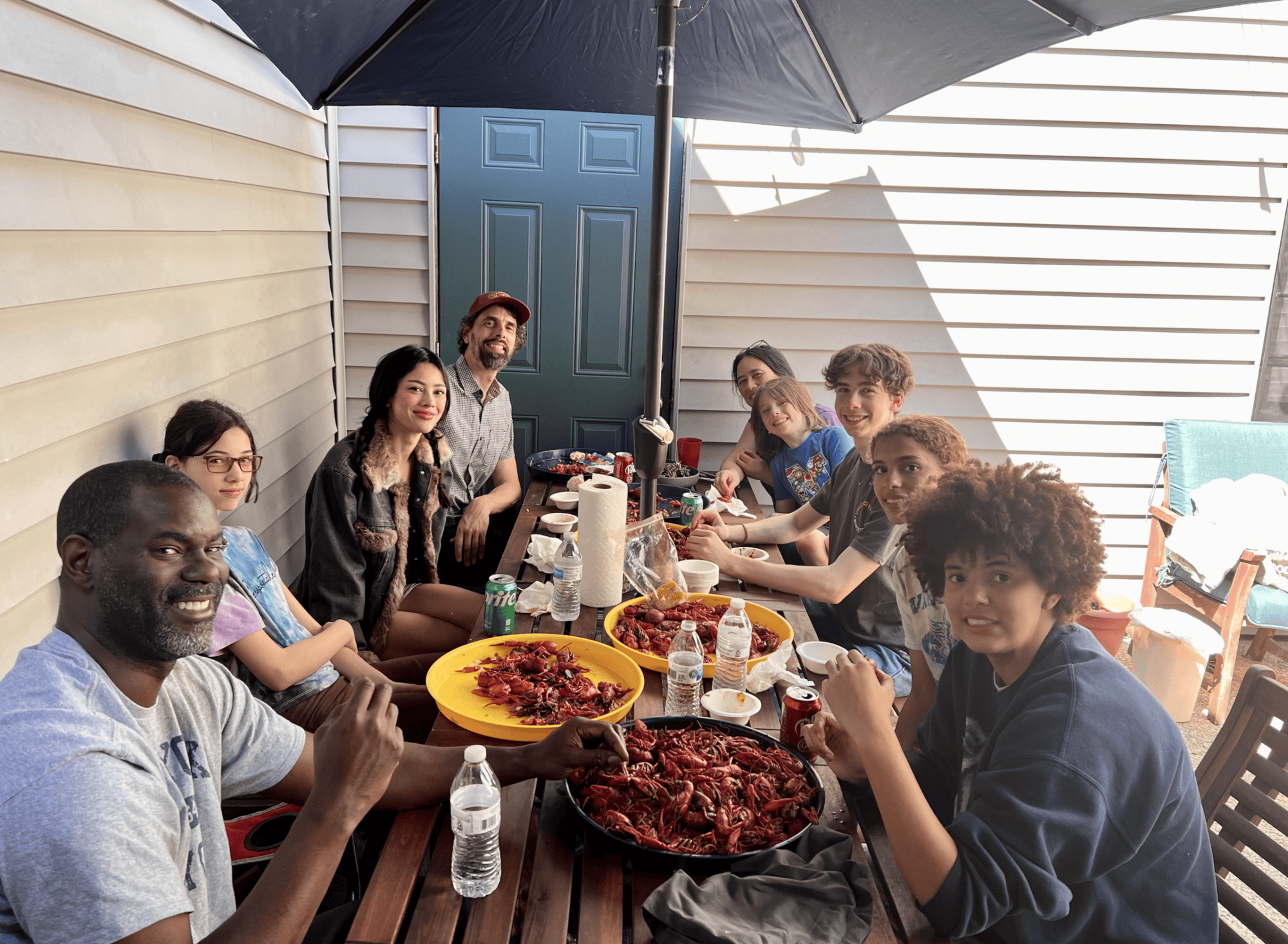 Group of diverse friends enjoying a backyard barbecue under a large umbrella.