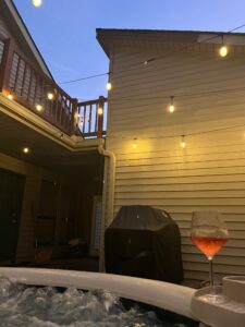 Cozy backyard scene with hot tub, string lights, and a glass of rosé wine.