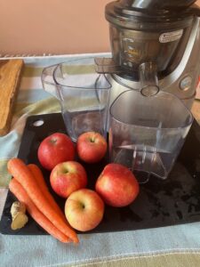 Fresh apples and carrots with juicer on kitchen counter.