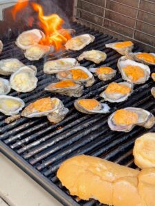Oysters being grilled on a barbecue with flames and a piece of bread nearby.