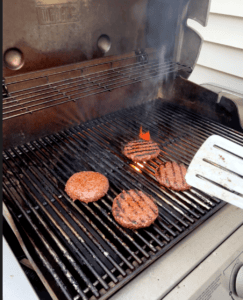 Grilling burgers on a barbecue grill with flames and smoke.