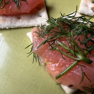 Homemade cured salmon on crackers topped with fresh dill, photographed in natural light.