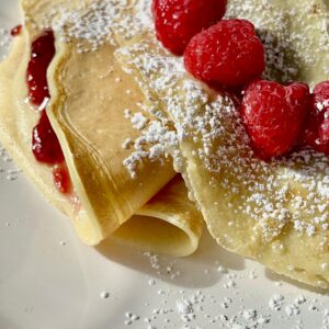 Delicious homemade crepes filled with raspberry jam, topped with fresh raspberries and powdered suga.