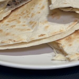 Delicious grilled quesadilla with melted cheese and savory filling on a white plate.