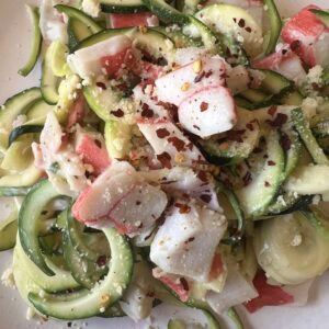 Fresh zucchini noodles with crab meat, garlic, and cheese, garnished with red pepper flakes.