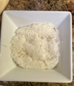 Steamed white rice served in a white square bowl on a kitchen countertop.