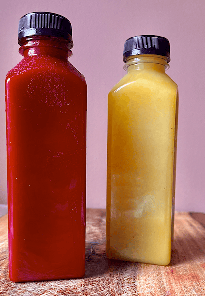Healthy homemade juice bottles with vibrant red and yellow liquids on wooden surface.