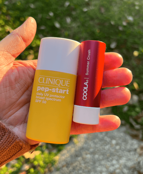 FSA eligble sun care: Clinique Pep-Start SPF 50 and Coola Summer Crush lip balm in hand.