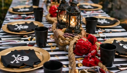 Pirate themed party table with skull napkins, lanterns, and red decorations.