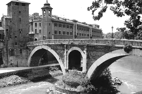 Historic stone bridge over a river in a cityscape, black and white photo.