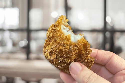 Delicious golden-brown croquette held in hand, showcasing crispy exterior and creamy filling.