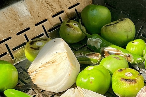 Fresh green tomatoes and sliced onion on a wire rack for cooking or preservation.