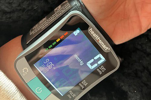 Digital wrist blood pressure monitor showing systolic, diastolic, and pulse readings with app connec.
