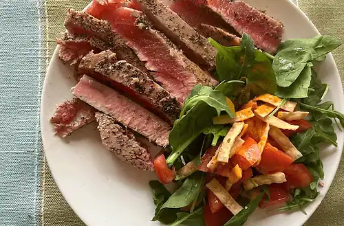 Juicy homemade steak with fresh greens and tomato salad on a white plate.