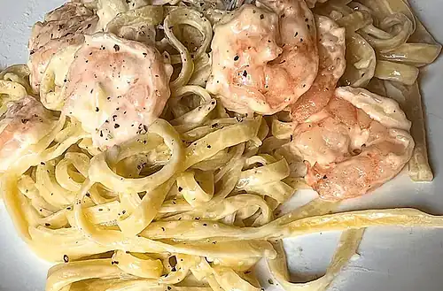 Creamy shrimp Alfredo served over fettuccine pasta with black pepper garnish.